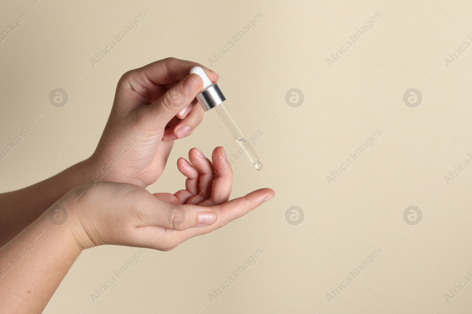 Photo of Woman applying cosmetic serum onto finger on beige background, closeup. Space for text