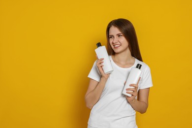 Photo of Beautiful young woman holding bottles of shampoo on yellow background. Space for text