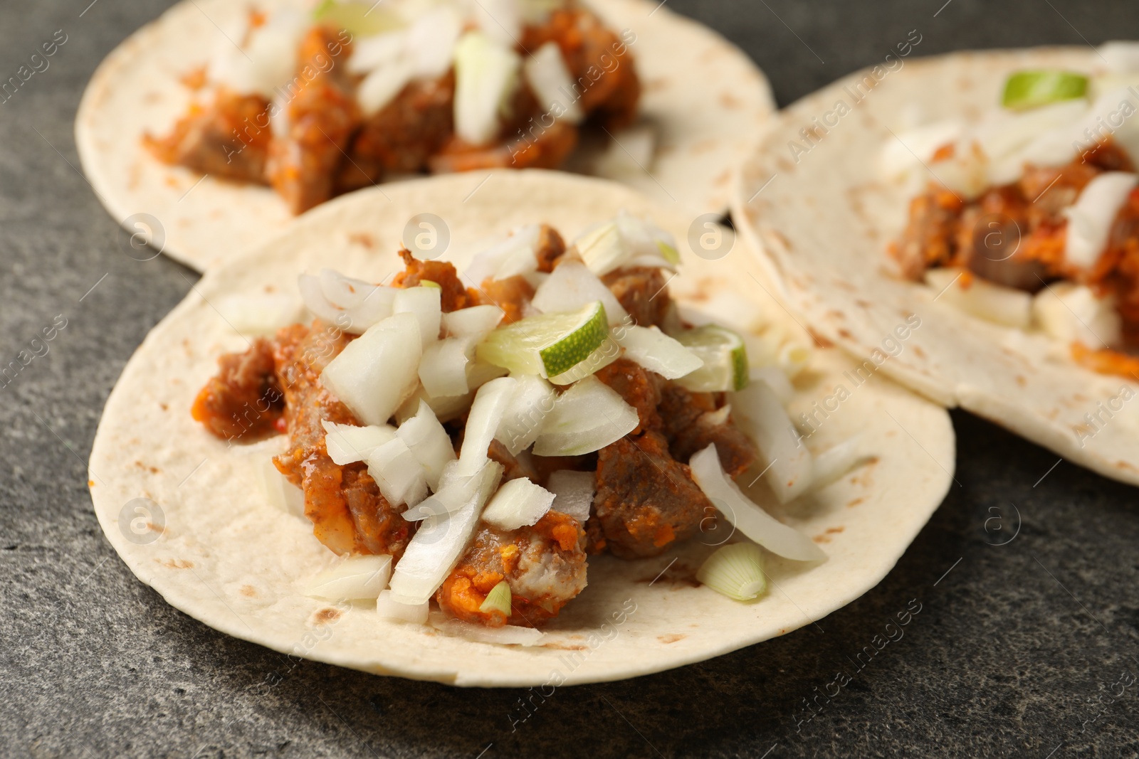 Photo of Delicious tacos with vegetables, meat and lime on grey textured table, closeup