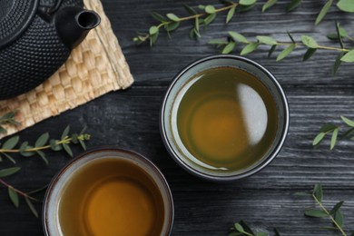 Photo of Aromatic eucalyptus tea on black wooden table, flat lay