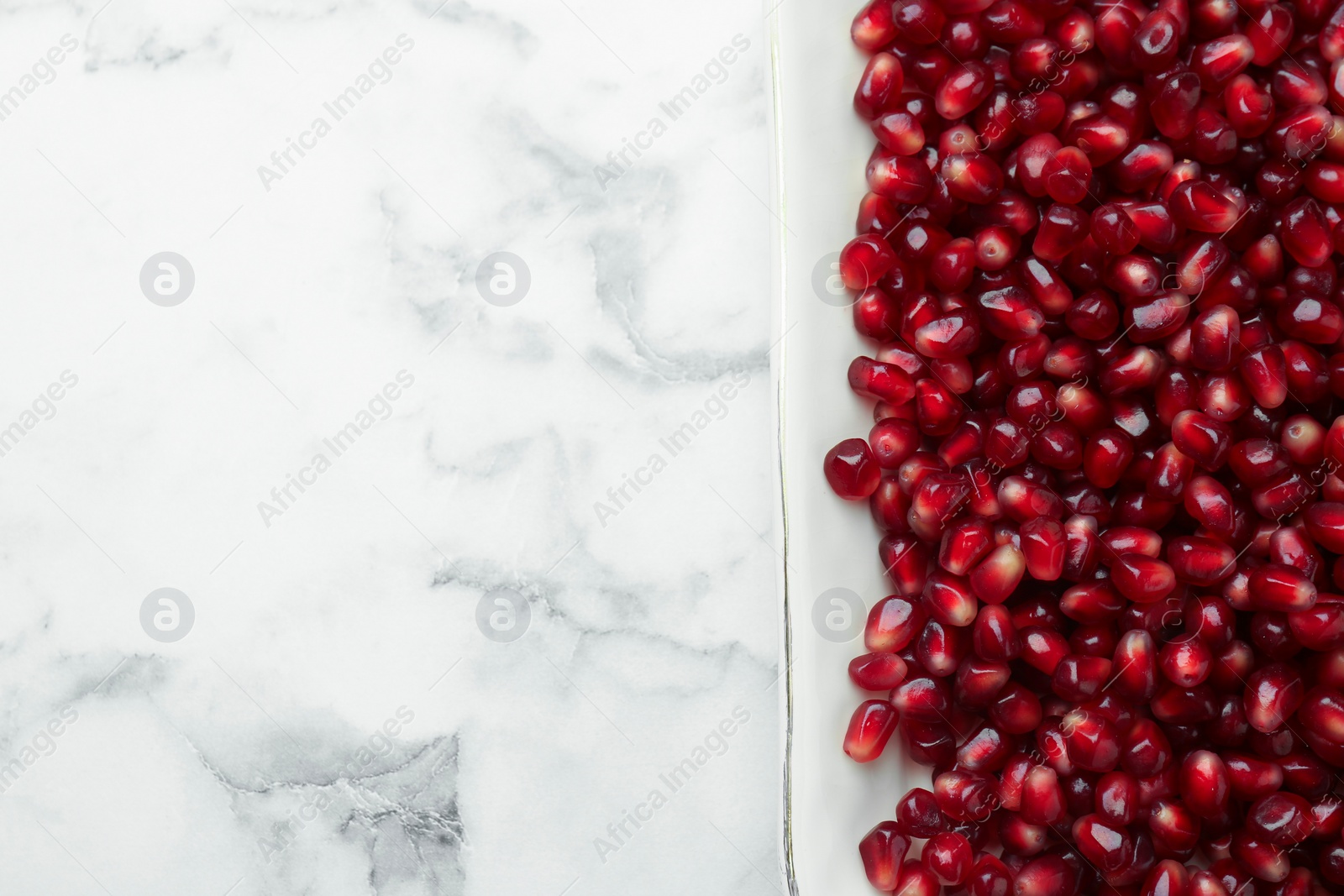 Photo of Ripe juicy pomegranate grains on white marble table, top view. Space for text