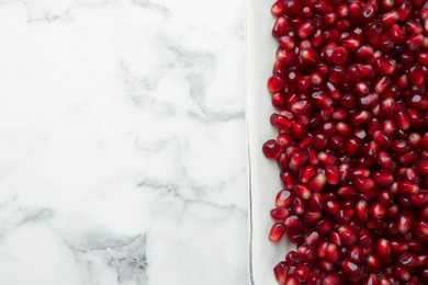 Photo of Ripe juicy pomegranate grains on white marble table, top view. Space for text