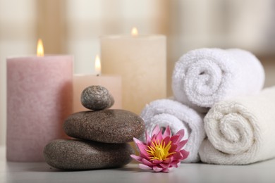 Photo of Spa composition. Burning candles, lotus flower, stones and towels on white table