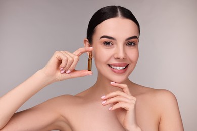 Beautiful young woman holding skincare ampoule on grey background