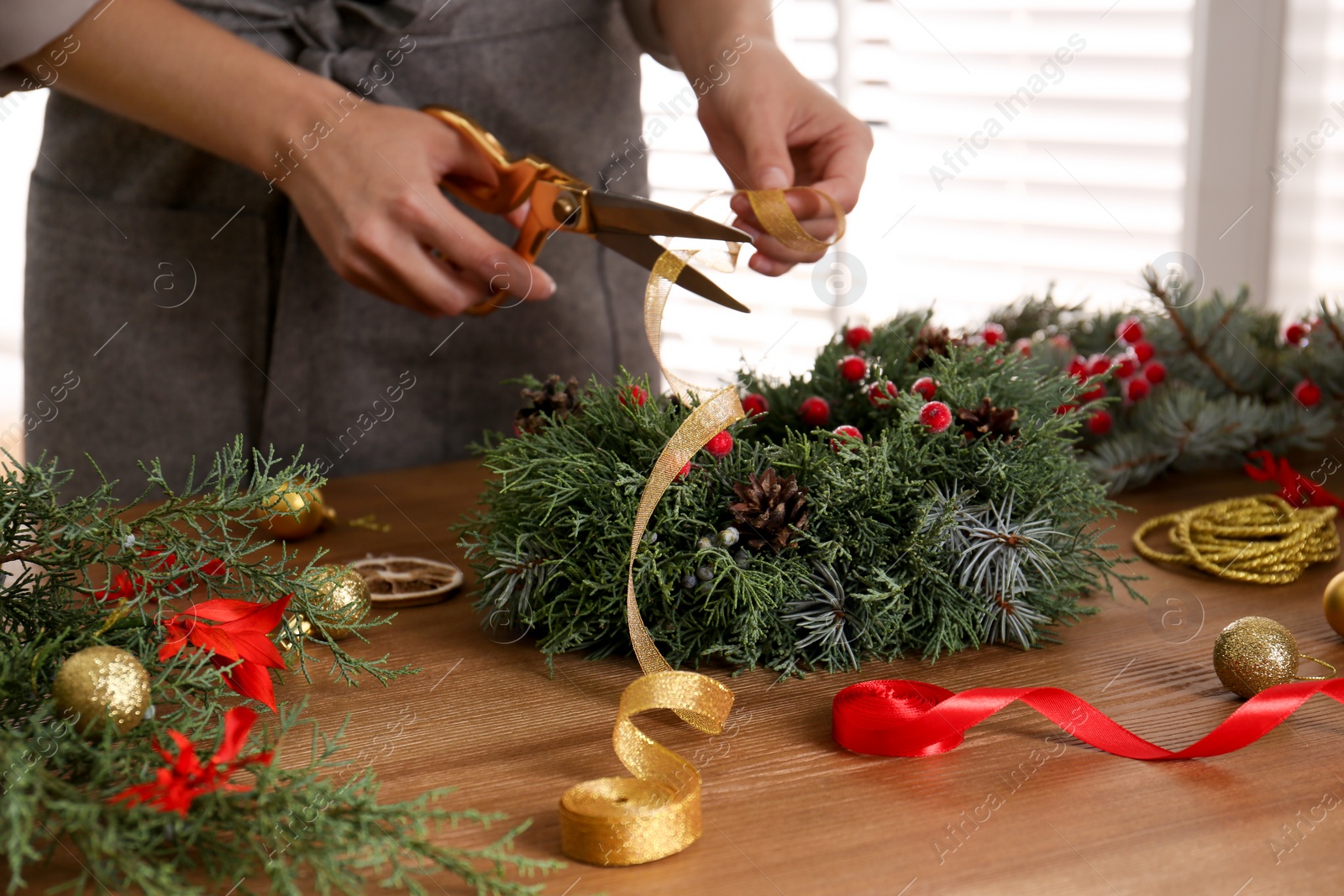 Photo of Florist making beautiful Christmas wreath at wooden table indoors, closeup