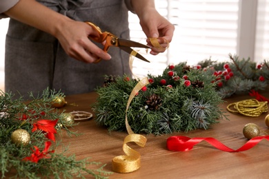 Florist making beautiful Christmas wreath at wooden table indoors, closeup