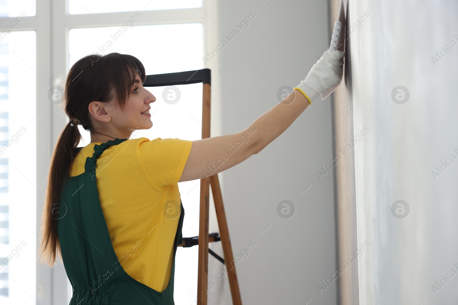 Photo of Woman smoothing stylish gray wallpaper in room