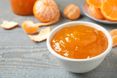 Tasty tangerine jam in bowl on grey wooden table. Space for text