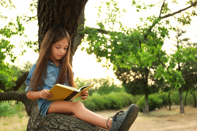 Cute little girl reading book on tree in park