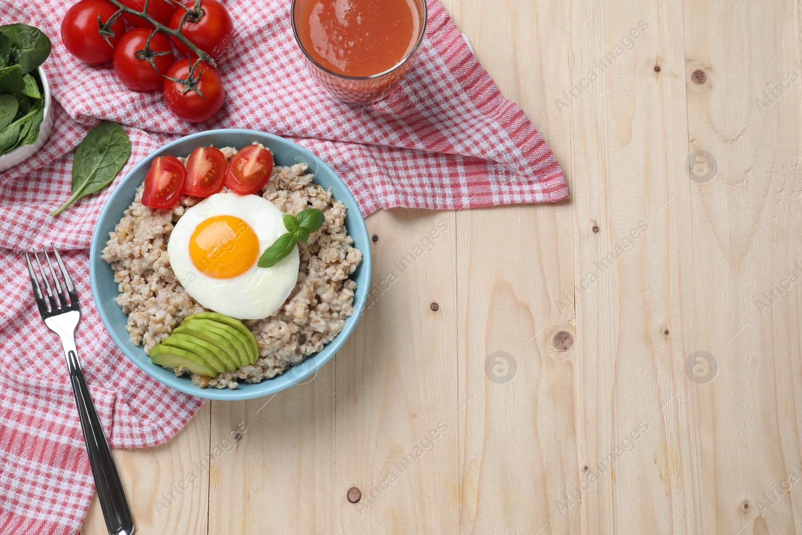 Photo of Delicious boiled oatmeal with fried egg, bacon, avocado and tomato served on wooden table, flat lay. Space for text