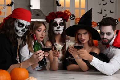 Photo of Group of people in scary costumes with cocktails celebrating Halloween indoors