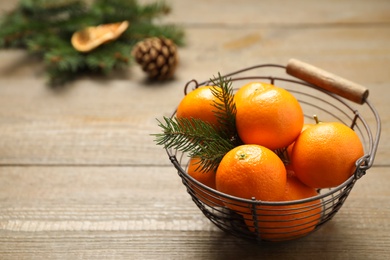 Photo of Fresh tangerines with fir tree branch in metal basket on wooden table, space for text. Christmas atmosphere