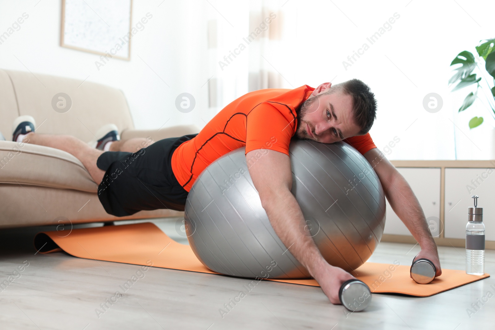 Photo of Lazy young man with sport equipment at home