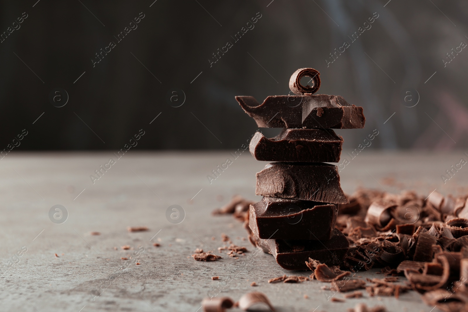 Photo of Curls and pieces of tasty chocolate on gray table. Space for text