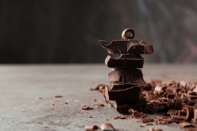 Photo of Curls and pieces of tasty chocolate on gray table. Space for text