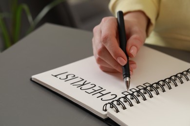Woman filling Checklist with pen at grey table, closeup