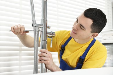Photo of Young plumber repairing faucet with spanner in bathroom