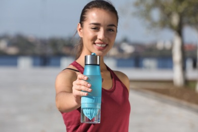 Photo of Young sporty woman holding bottle of water outdoors on sunny day