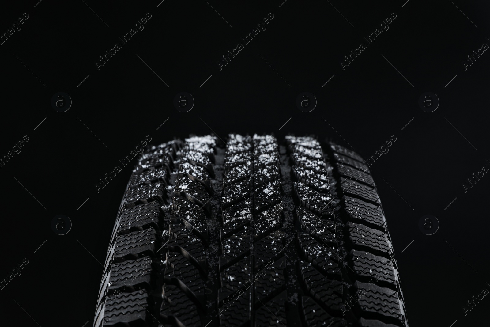 Photo of Snowy winter tire on black background, closeup