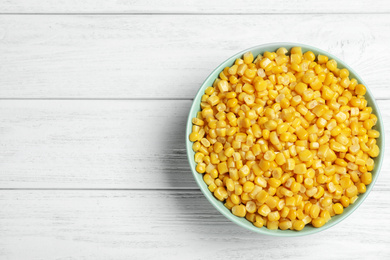 Photo of Delicious canned corn in bowl on white wooden table, top view. Space for text