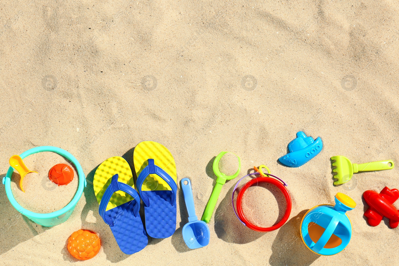 Photo of Flat lay composition with plastic beach toys on sand. Space for text