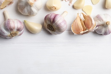 Fresh organic garlic on white wooden table, flat lay. Space for text