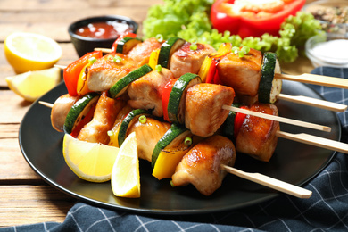 Delicious chicken shish kebabs with vegetables and lemon on wooden table, closeup