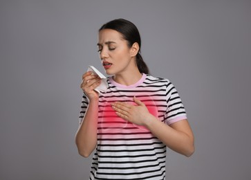 Young woman with tissue coughing on grey background. Cold symptoms