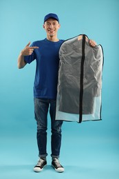 Photo of Dry-cleaning delivery. Happy courier holding garment cover with clothes on light blue background