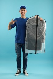 Dry-cleaning delivery. Happy courier holding garment cover with clothes on light blue background