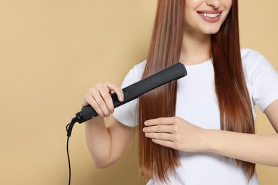 Photo of Young woman using hair iron on beige background, closeup. Space for text