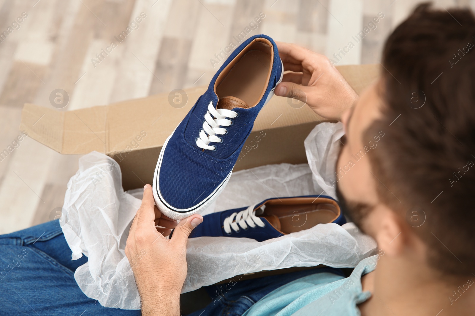 Photo of Young man opening parcel with shoes at home, closeup