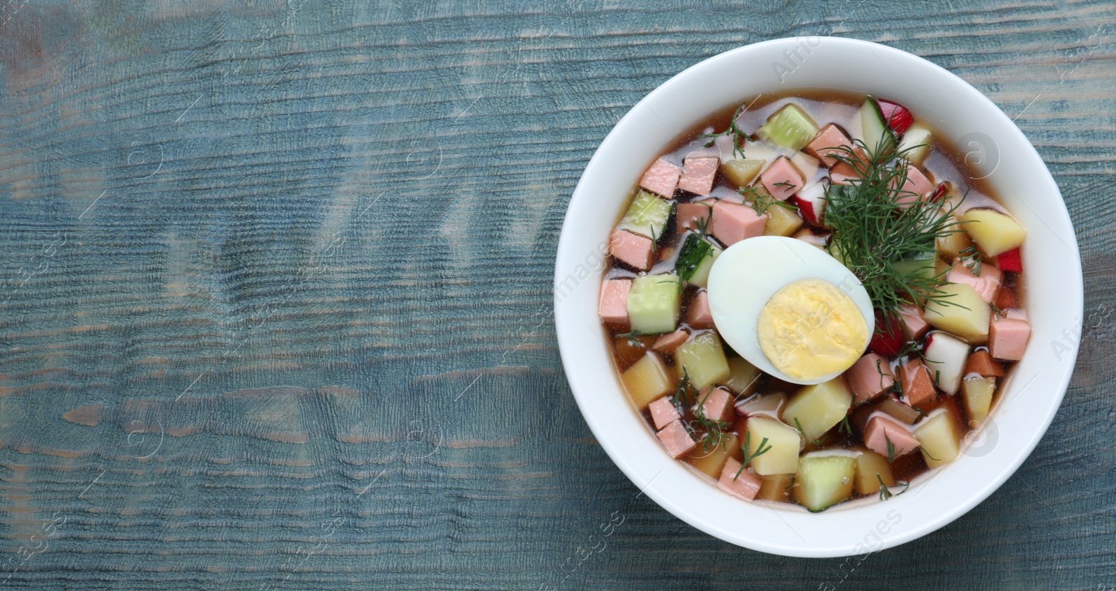 Photo of Delicious cold okroshka with kvass and space for text on blue wooden table, top view. Traditional Russian summer soup