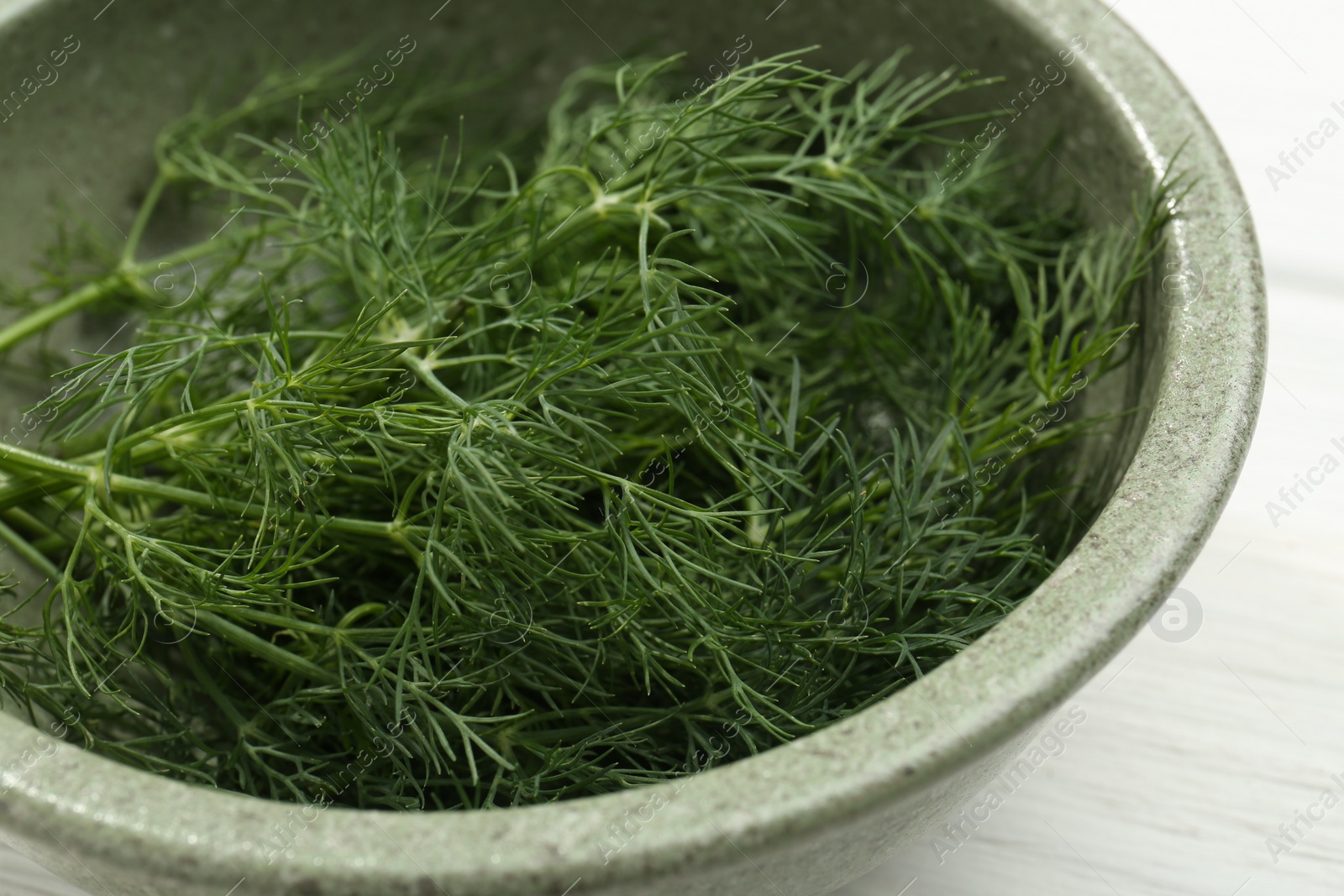 Photo of Bowl of fresh green dill on white wooden table, closeup