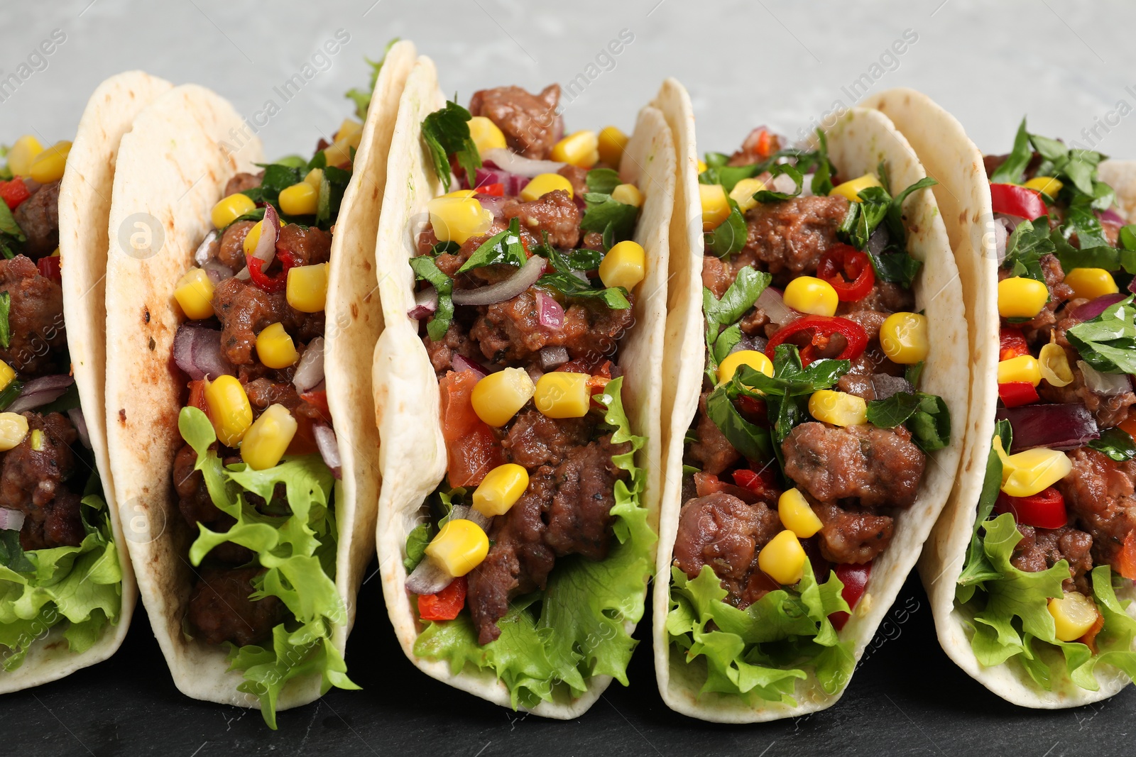 Photo of Delicious tacos with meat and vegetables on table, closeup