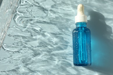 Photo of Wet bottle of cosmetic serum on light blue background, top view