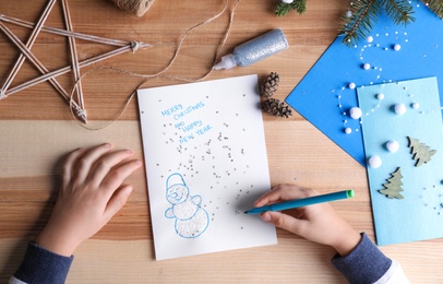 Photo of Little child making Christmas card at wooden table, top view