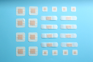 Photo of Different types of sticking plasters on light blue background, flat lay