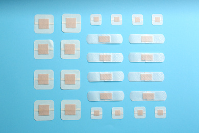 Different types of sticking plasters on light blue background, flat lay