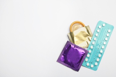 Condoms and birth control pills on light grey background, flat lay with space for text. Safe sex concept