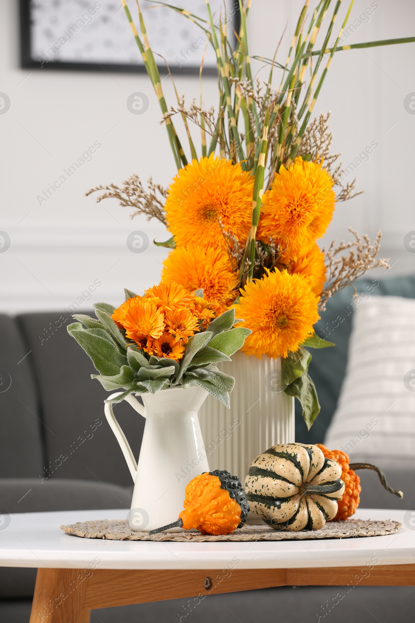 Photo of Beautiful bouquets with bright orange flowers and pumpkins on coffee table indoors. Autumn vibes