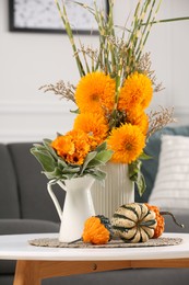 Beautiful bouquets with bright orange flowers and pumpkins on coffee table indoors. Autumn vibes