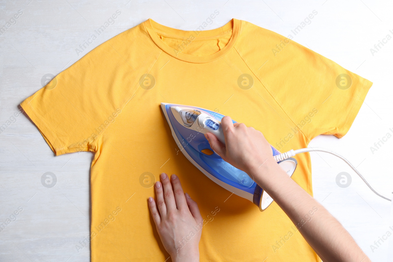 Photo of Woman ironing t-shirt on light background, top view