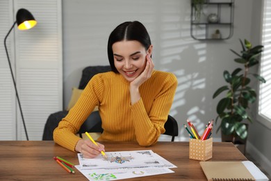 Photo of Young woman coloring antistress page at table indoors