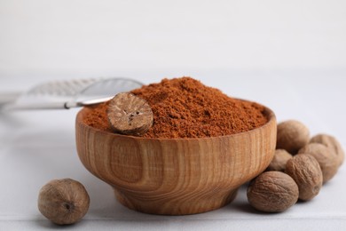 Nutmeg powder in bowl and seeds on white table