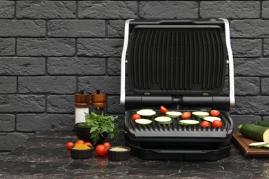 Photo of Electric grill with vegetables and spices on black marble table