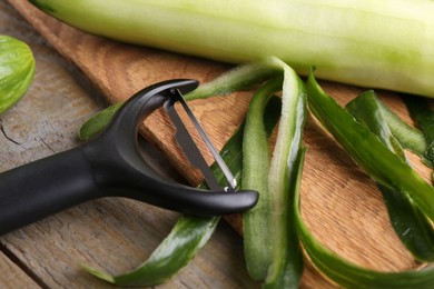 Photo of Fresh cucumber, peels and peeler on wooden table, closeup