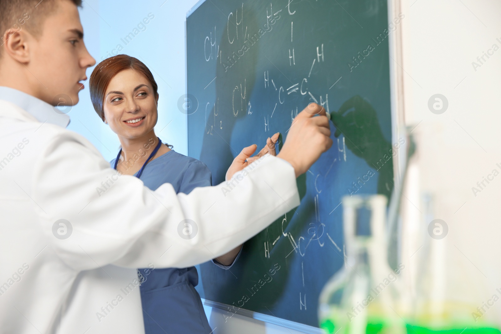 Photo of Scientists writing chemical formulas on chalkboard indoors