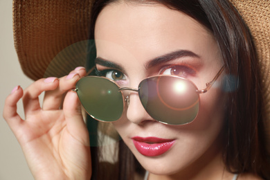 Beautiful woman in stylish sunglasses and hat on beige background