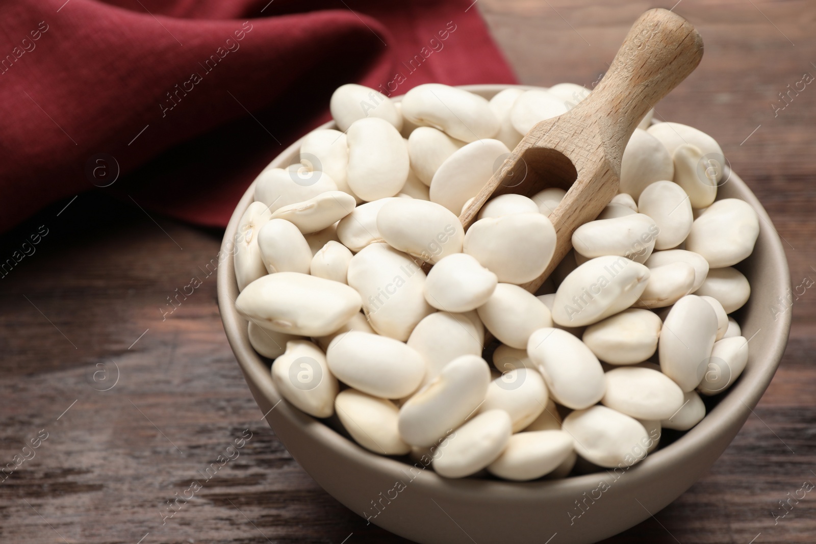 Photo of Raw white beans and scoop in bowl on wooden table, closeup